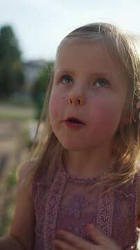 A beautiful little girl eats a popsicle. A happy and joyful child in stylish clothes enjoys eating a ice cream, discussing the taste, smiling, and expressing her taste sensations. Vertical Video