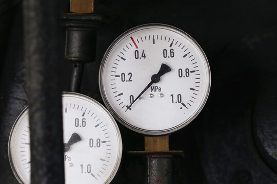 Analog pressure gauges measure industrial system. Round dials display values in megapascals. Metal pipes connect measuring instruments. Technical equipment forms engineering background.