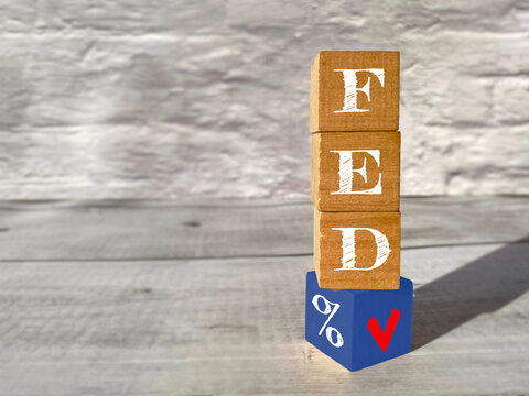 Wooden blocks spelling FED with a percentage symbol and downward arrow, representing a Federal Reserve interest rate cut, monetary policy and declining interest rates.
