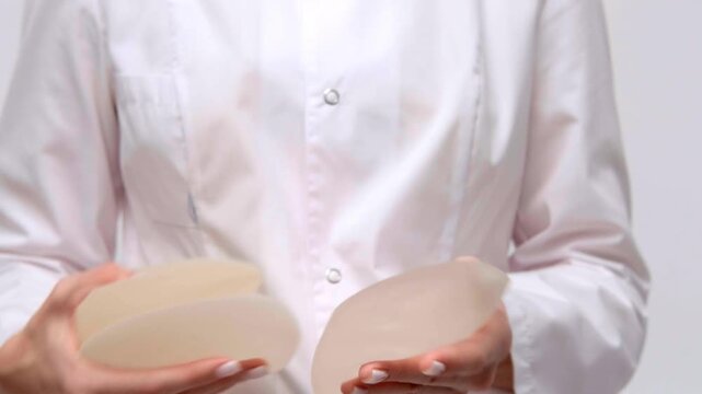 A doctor demonstrating two silicone breast implants in a medical office, plastic surgery consultation, patient care, healthcare.