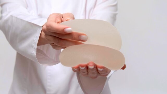 A medical specialist presenting a pair of breast implants, plastic surgery consultation, healthcare marketing, patient education.