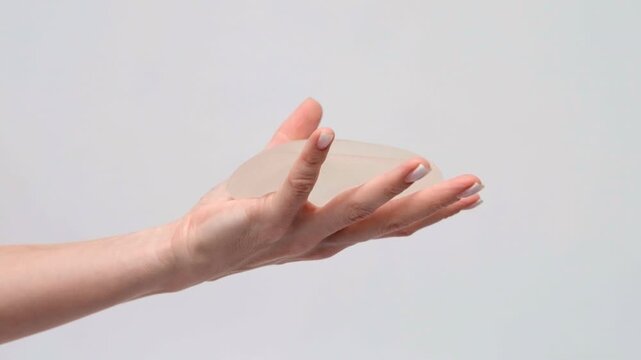 A hand holding a silicone breast implant on a neutral background, plastic surgery presentation, medical consultation, healthcare.