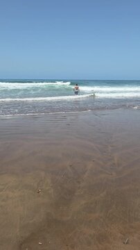 Gentle ocean waves washing over a sandy shoreline beneath a clear blue sky, creating a peaceful coastal scene.