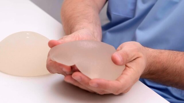 Plastic surgeon squeezing a silicone breast implant to demonstrate flexibility and durability, healthcare advertising, plastic surgery, medical equipment.