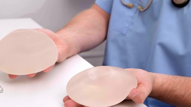 Plastic surgeon holding silicone breast implants to demonstrate elasticity and quality during a medical consultation, healthcare advertising, plastic surgery, patient care.