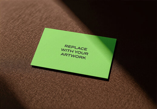 Business card mockup on textured brown fabric surface with directional lighting, flat lay presentation, horizontal stationery branding template for graphic design and print