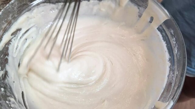 Mixing thick, white, creamy batter with a metal whisk in a bowl during the homemade cooking process