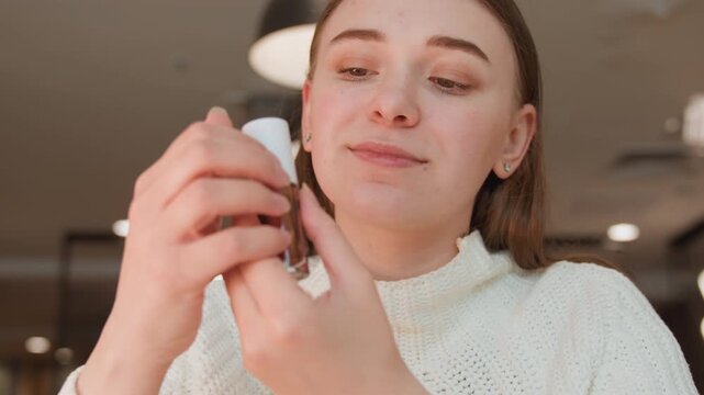Close frontal view of young woman in modern interior lifting dropper from cosmetic bottle above open palm, showing gentle downward motion, careful handling, soft light, and calm beauty routine