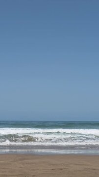 Peaceful Atlantic Ocean waves rolling onto a sandy beach under a clear blue sky.