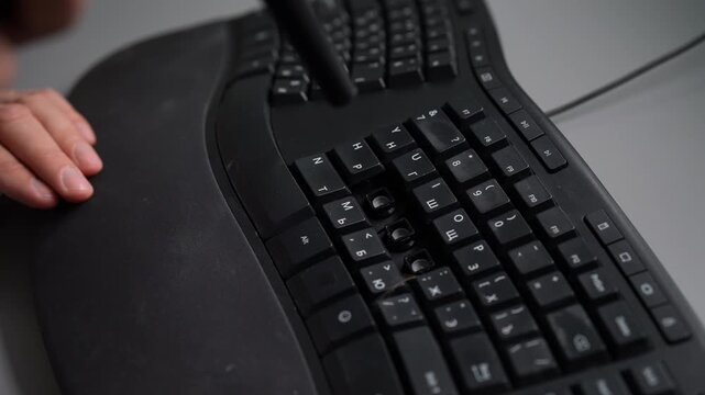 Service center worker disassembling and cleaning dusty ergonomic computer keyboard by removing keycaps and blowing out dirt and debris with air duster can.