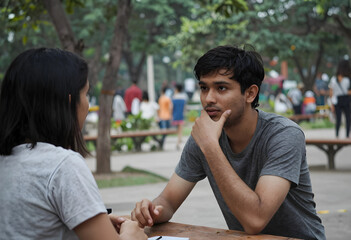 Fototapeta premium Deep conversation and active listening, young man with thoughtful expression talking to a woman outdoors in a park setting
