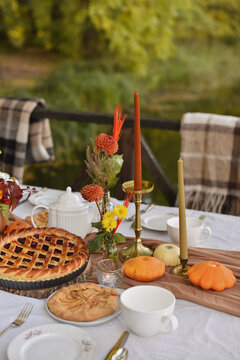 Cozy autumn Thanksgiving table setting outdoors with homemade pies, candles, and pumpkins