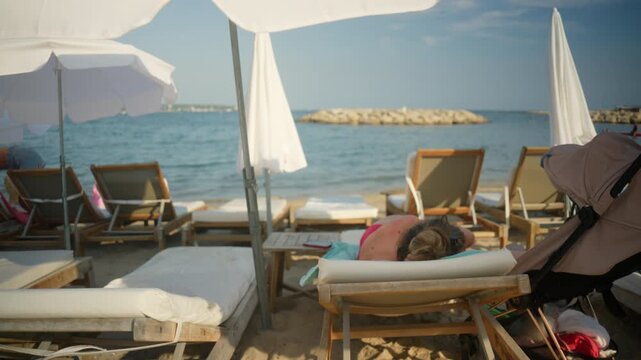 Woman enjoying a peaceful summer vacation, relaxing on a sunbed under an umbrella at a sandy beach resort by the clear sea