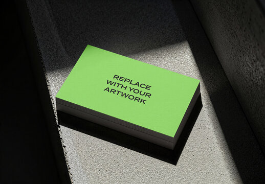 Stacked business card mockup with green cover and black text on a concrete surface, angled view natural light shadows, realistic stationery branding presentation, commercial graphic design template