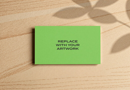 Business card mockup on a wooden surface with leaf shadow, flat lay stationery design display, minimalist print template for branding presentation, natural light interior workspace