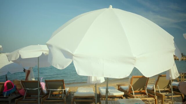 White beach umbrella on a sunny day providing shade, with lounge chairs and the ocean in the background, creating a relaxing summer scene