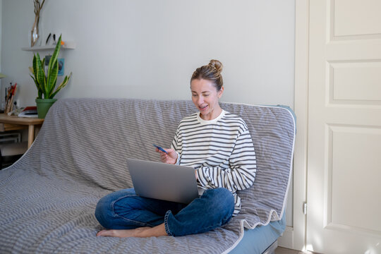 Cheerful woman purchasing online at e-commerce shop website from home using laptop and credit card, smiling female enjoys digital shopping on computer, making online payment, confirming purchase.