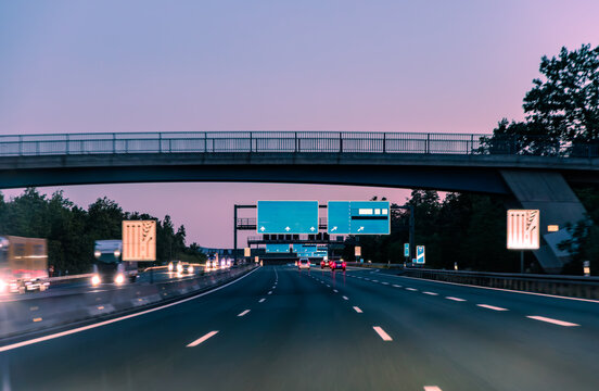 Driving on highway at twilight with blank blue directional signs and bridge, generic highway transport and logistics concept