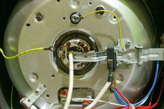 Exposed motor with wiring and metal components from rice cooker. Yellow wire connects to central housing. White and colored wires run alongside metal brackets. Industrial interior shows mechanical com