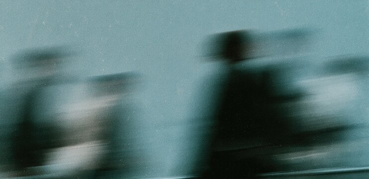Motion blurred figures in a cool, hazy light against a soft, muted background