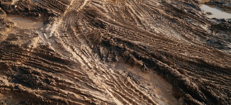 Textured brown mud with deep tire tracks and puddles
