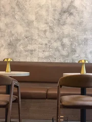 Fotobehang Horeca Empty cafe interior with two tables, chairs, brown seating, and a plain empty wall. Vertical lifestyle photo in a cozy restaurant atmosphere. Cafe interior, minimalist style and no people  © onajourney