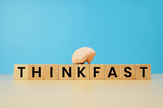 Think fast concept with wooden letter blocks and miniature human brain model on blue background, representing quick thinking, intelligence, decision making and cognitive skills.