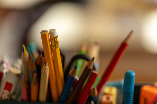 Gros plan sur un assortiment de crayons color&eacute;s et de fournitures d'&eacute;criture dans un pot, avec une salle de classe floue en arri&egrave;re-plan, &eacute;voquant la rentr&eacute;e scolaire et la cr&eacute;ativit&eacute;.