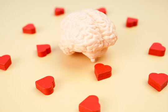 Human brain model surrounded by red hearts on yellow background, representing emotional intelligence, love, mental wellness, psychology, empathy and positive emotions.