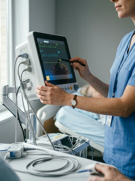 Clinician in blue scrubs using a stylus on a bedside heart monitor screen