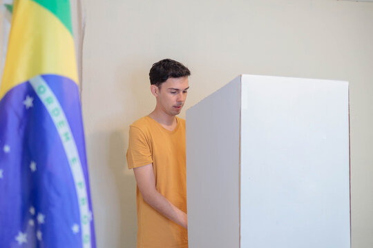 Jovem eleitor vota na cabine eleitoral, com a bandeira do Brasil desfocada em primeiro plano, durante as elei&ccedil;&otilde;es presidenciais de outubro.