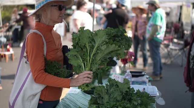 A senior woman smiles while selecting fresh greens at the Fort Bragg Farmers Market in Northern California near Mendocino.