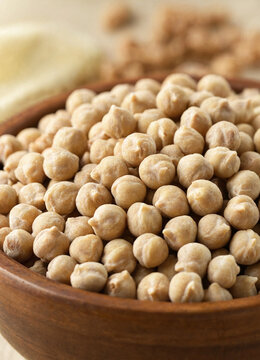 A wooden bowl filled with dried chickpeas fills the frame, showing texture and natural color with a soft blurred background.