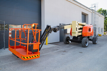 Industrial aerial work platform cherry picker with open personnel cage and articulated boom mechanism parked at site facility © K
