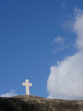 White cross is on a hilltop in front of a blue sky