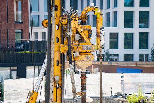 Yellow hydraulic rotary drilling rig mast with kelly bar drive head and auger drill bit operating on urban foundation construction site