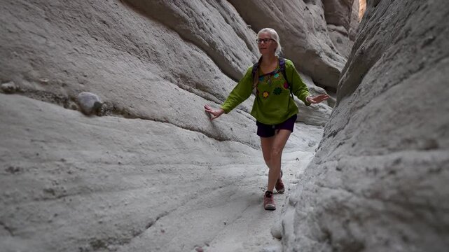 Happy mature woman hikes through a slot canyon in Anza Borego State Park, exploring the beauty of the California desert landscape.