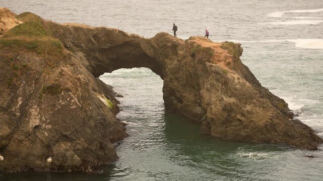 A couple enjoys the views while exploring the arch at Mendocino Headlands State Park on a foggy day near the coastline.