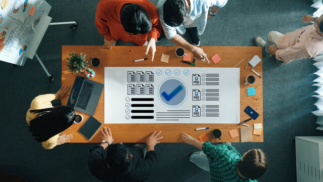 A diverse group of professionals engages in collaborative project management at a modern office table, utilizing laptops, sticky notes, and coffee cups for productive brainstorming sessions. Gantry
