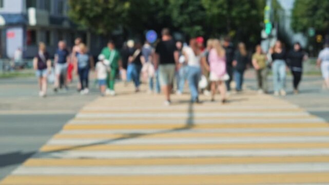 Defocus diverse group of people including men and women walk together across a pedestrian crossing in a bustling city