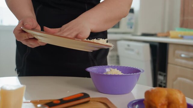 Adult hands guide sieve over purple mixing bowl on bright kitchen countertop, releasing fine flour cloud beside utensils and cutting board; soft motion suggests careful home baking prep