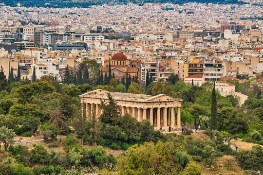 Panoramic high-angle view of the Temple of Hephaestus surrounded by green trees and urban Athens.