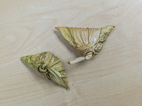 Two traditional ketupat palas made of glutinous rice wrapped in palm leaves rest on a smooth wooden table background.