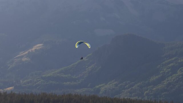 Aerial close up paragliding over San Juan National Forest in southern Colorado with person flying with a colorful wing through heavily forested mountains in summer
