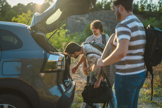Friends packing luggage into car trunk for road trip adventure