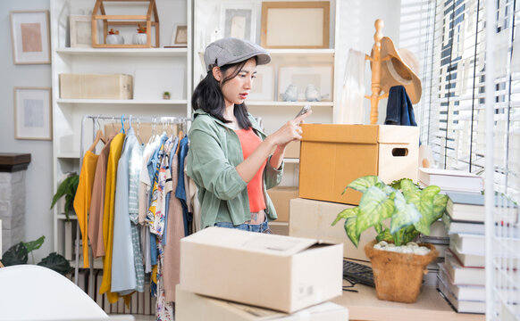 Small business owner taking a photo of a cardboard shipping parcel with her smartphone to update product delivery status.