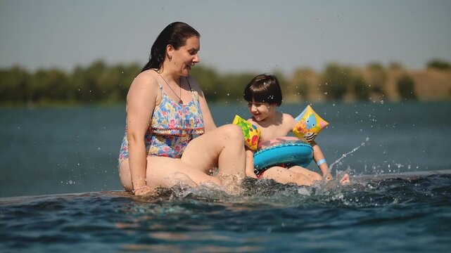 Mother and Little Son Sitting on Pool Edge Splashing Water and Giving High Five