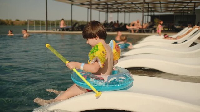 Little Boy Playing with Water Blaster Gun in Swimming Pool