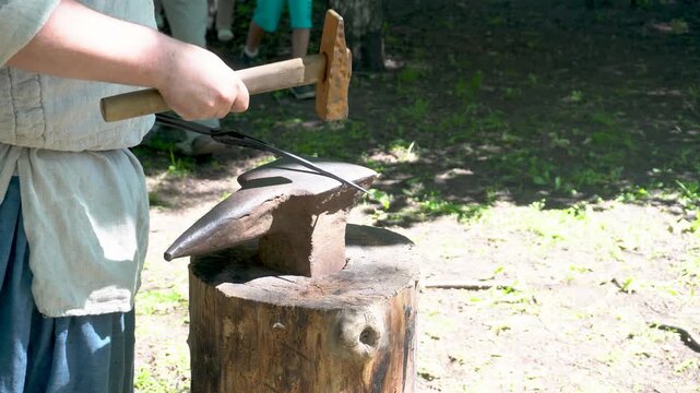 A blacksmith is crafting a metal item by hammering a hot metal workpiece on an anvil. 4k video shot.
