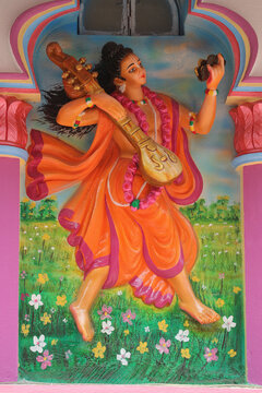 Colorful stone wall relief carving of the ancient sage Narada Muni holding a veena musical instrument.